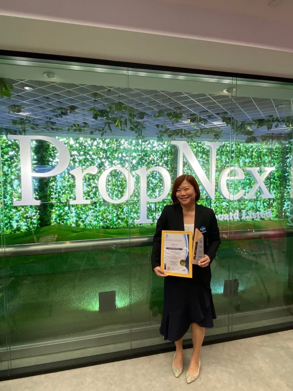 Karen Lim with a certificate at the PropNex office wall